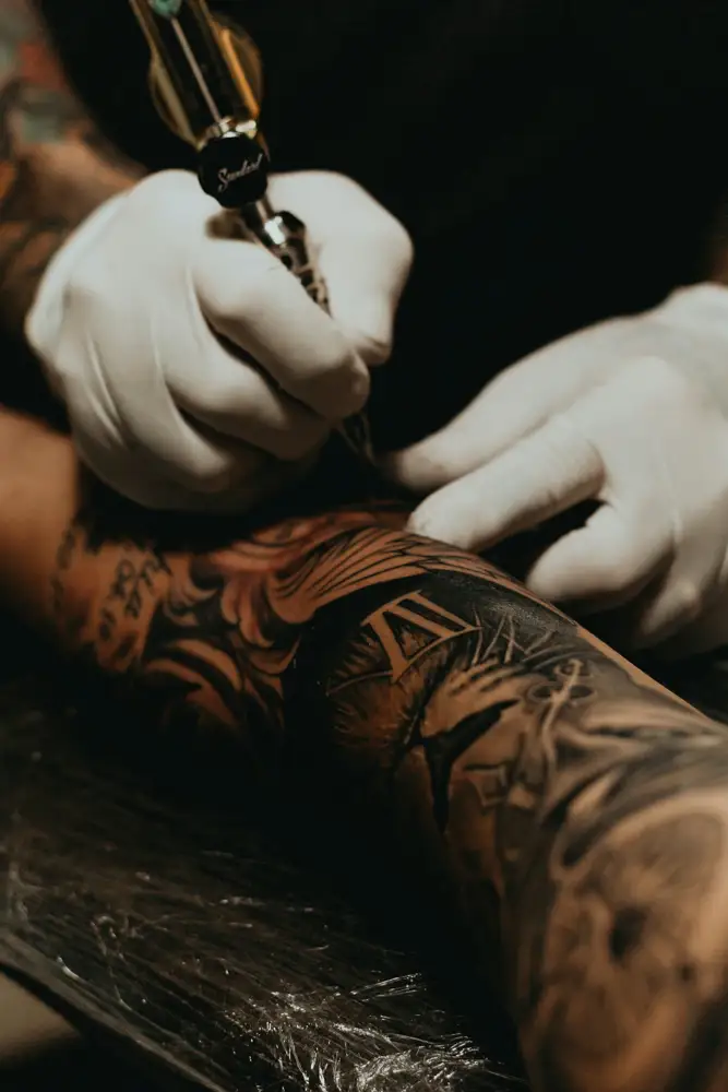 Tatuador trabajando un brazo con guantes blancos